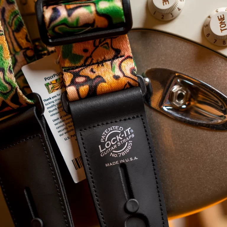 Close-up of a camouflage-pattern guitar strap with black leather ends and metal hardware, showing the Lock-It strap logo. ขายราคาพิเศษ