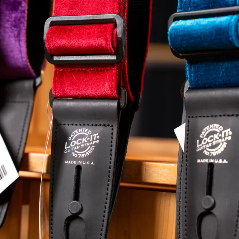 Close-up of red and blue padded guitar straps with black leather ends labeled 'Lock-It Guitar Straps' and 'Made in U.S.A.' on a wooden display. ขายราคาพิเศษ