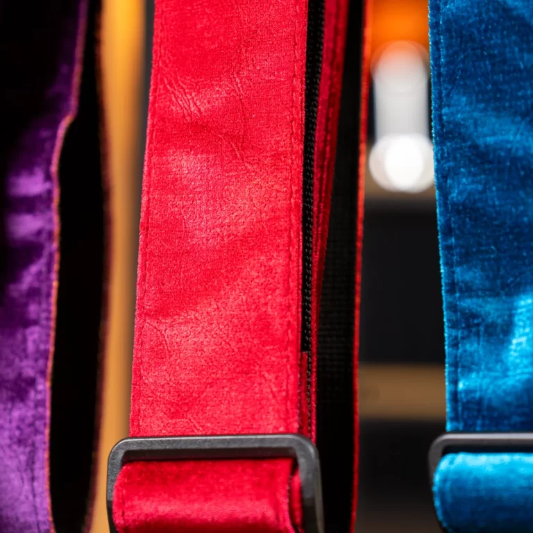 Close-up of red velvet backpack strap with a black buckle, flanked by purple and blue straps. ขายราคาพิเศษ