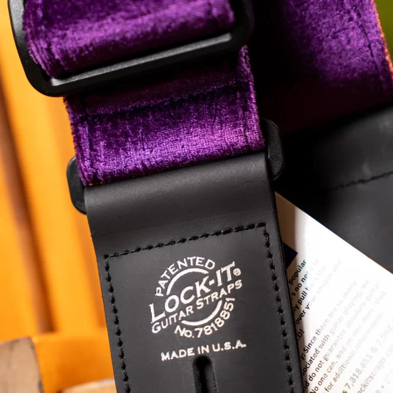 Close-up of a purple velvet guitar strap with black leather ends, featuring the patent label 'Lock-It Guitar Straps' and 'Made in USA'. ขายราคาพิเศษ