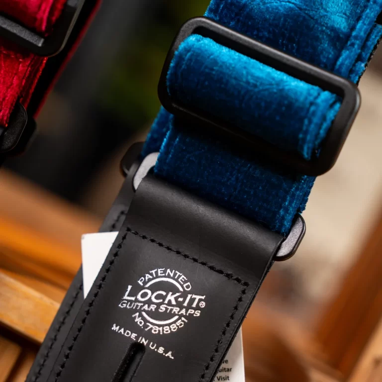 Close-up of a blue velvet guitar strap with a black leather end and buckle, showing the Lock-It brand label. ขายราคาพิเศษ