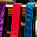 Three velvet sashes in purple, red and blue hanging over a wooden rod. ขายราคาพิเศษ