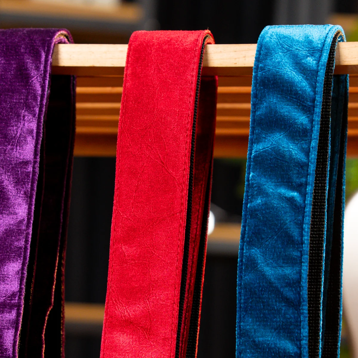 Three velvet sashes in purple, red and blue hanging over a wooden rod.