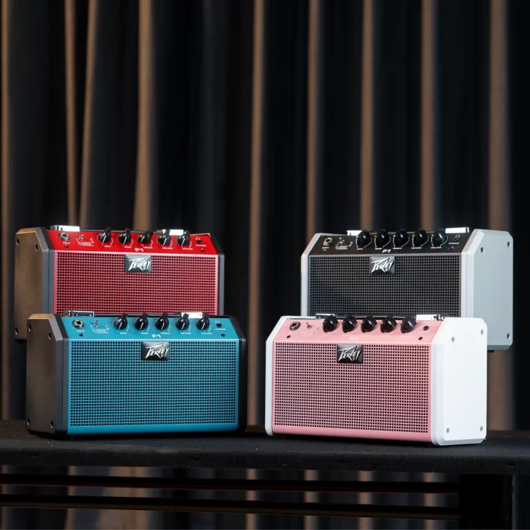 Four compact guitar amplifiers in red, teal, pink, and gray/white, arranged on a table against a dark curtain background. ขายราคาพิเศษ
