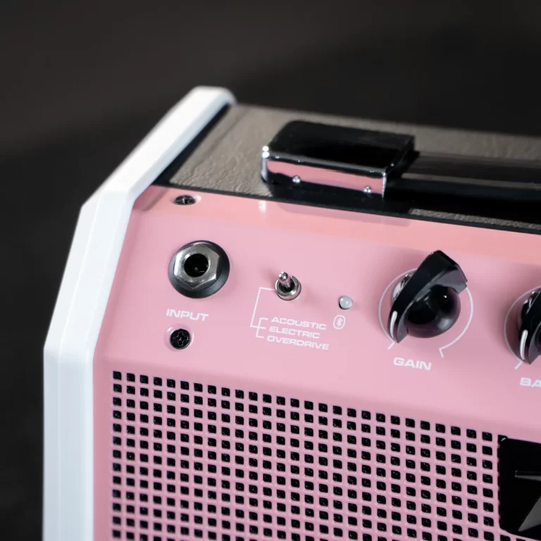 Close-up of a pink portable guitar amplifier showing the input jack, a small toggle, and a Gain knob on the top panel with a perforated grille below. ขายราคาพิเศษ