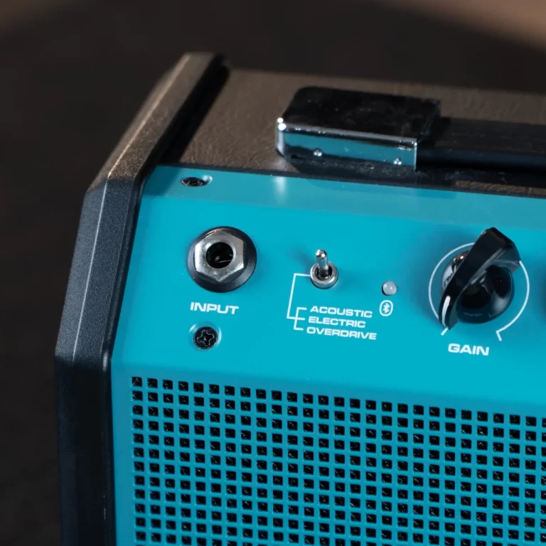 Close-up of a teal guitar amplifier front panel showing the INPUT jack, a small toggle switch, a gain knob, and the 'ACOUSTIC ELECTRIC OVERDRIVE' label over a perforated grille area. ขายราคาพิเศษ