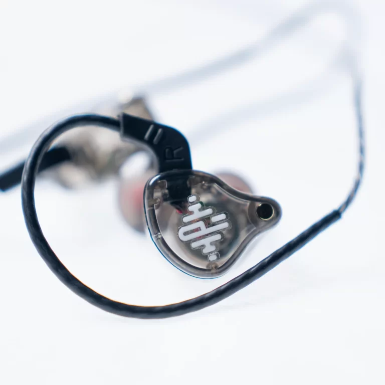 Close-up of a transparent in-ear monitor (earbud) with a black cable on a light surface, showing the inner housing through the shell. ขายราคาพิเศษ