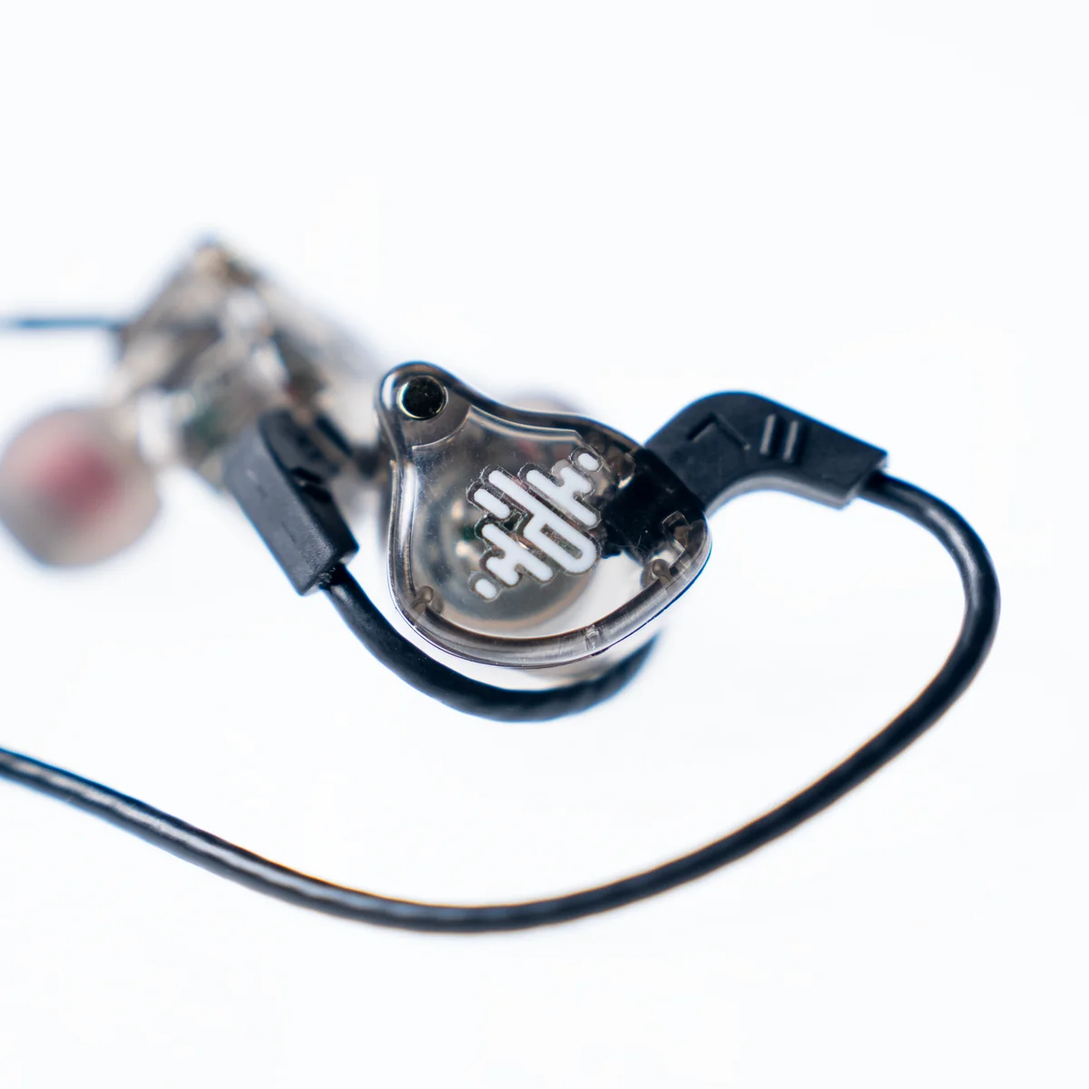 Close-up of a transparent in-ear monitor earphone with a black cable on a white background.