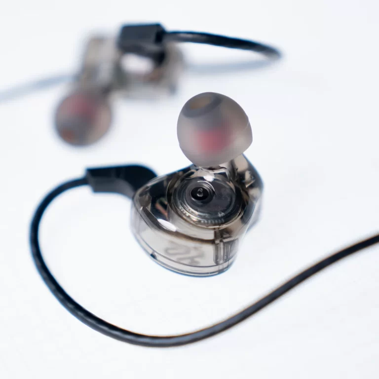 Close-up of a transparent in-ear monitor earbud with a soft silicone tip and black cable on a white surface ขายราคาพิเศษ