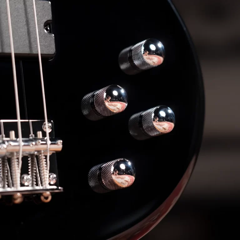 Close-up of four chrome control knobs on a black electric guitar body, with part of the bridge in view. ขายราคาพิเศษ