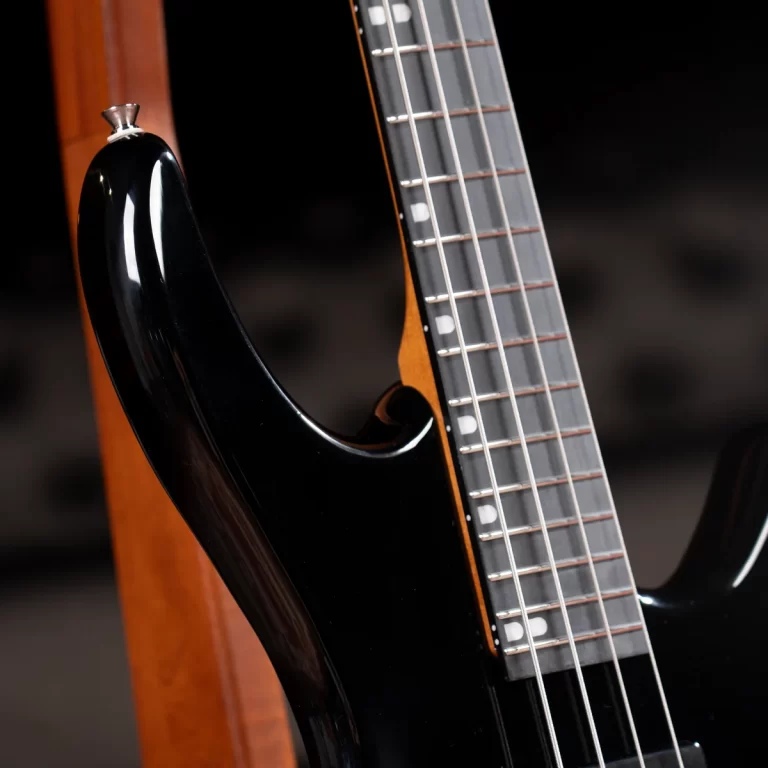 Close-up of a black electric bass guitar body and neck with strings and frets. ขายราคาพิเศษ