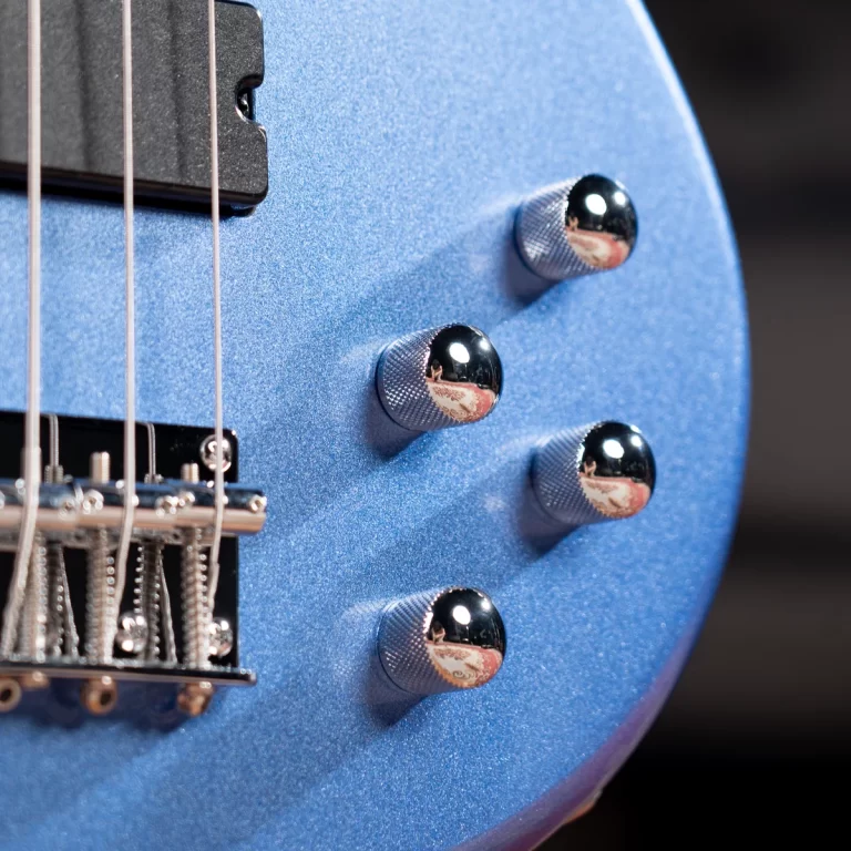 Close-up of a metallic blue electric guitar body with four chrome knurled control knobs and part of the bridge and strings visible. ขายราคาพิเศษ