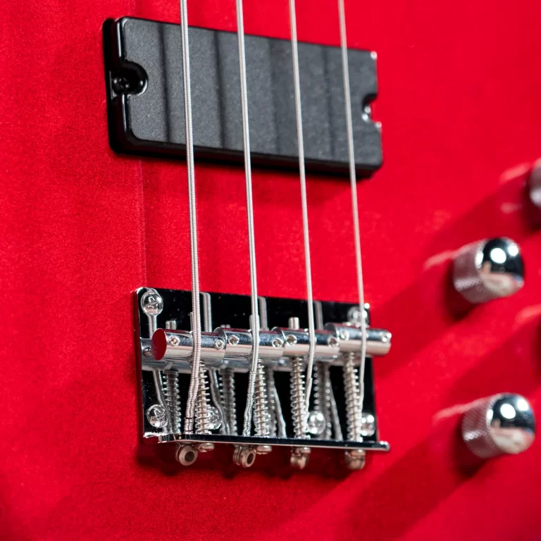 Close-up of a chrome guitar bridge on a red electric guitar with metal strings and control knobs nearby ขายราคาพิเศษ
