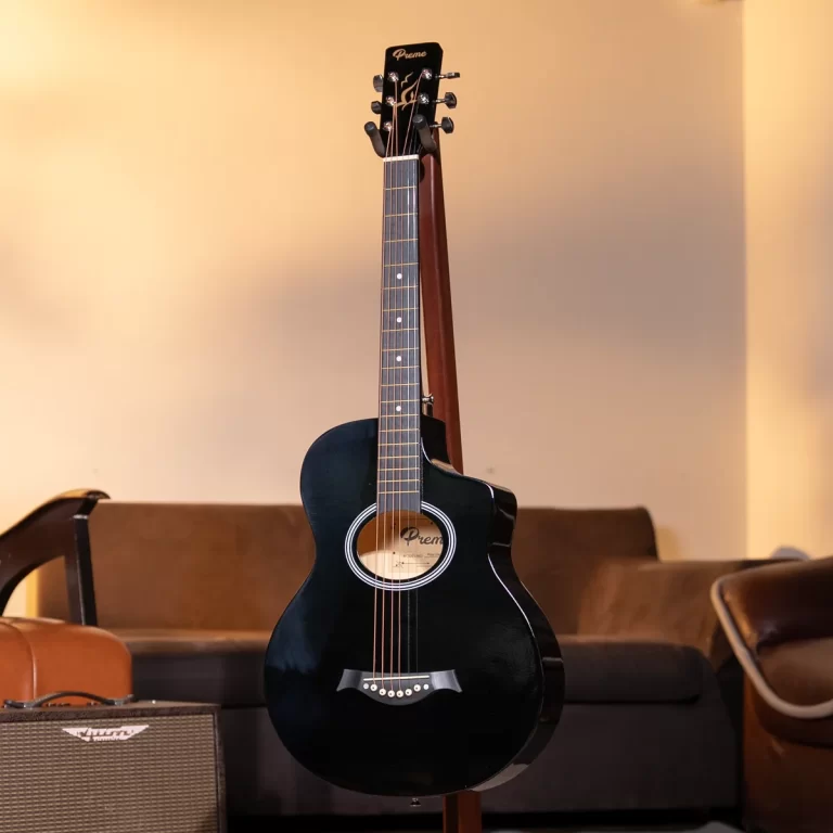Black acoustic guitar on a stand in a cozy living-room setting with a sofa and an amplifier nearby. ขายราคาพิเศษ