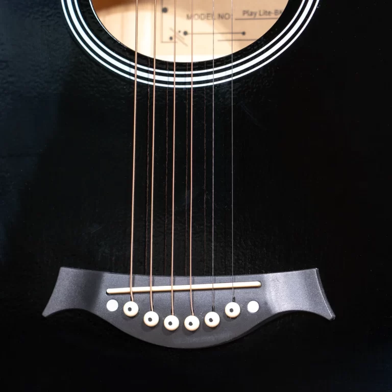 Close-up of a black acoustic guitar body showing six strings and bridge pins. ขายราคาพิเศษ