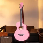 Pink acoustic guitar on a stand in a cozy living room, with a brown sofa and an amp nearby. ขายราคาพิเศษ