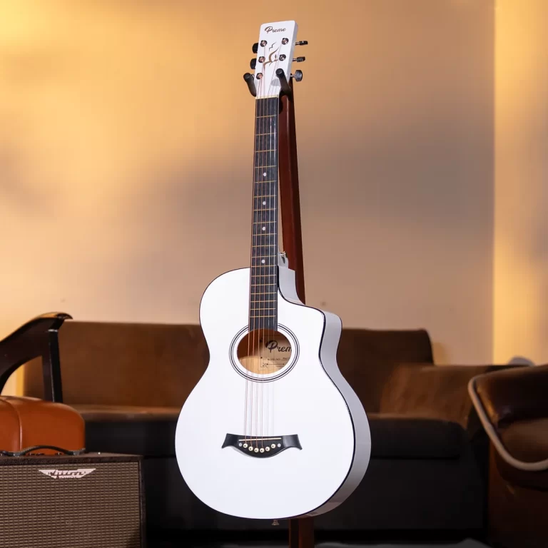 White acoustic guitar on a stand in a cozy living room with warm lighting and a brown sofa in the background. ขายราคาพิเศษ