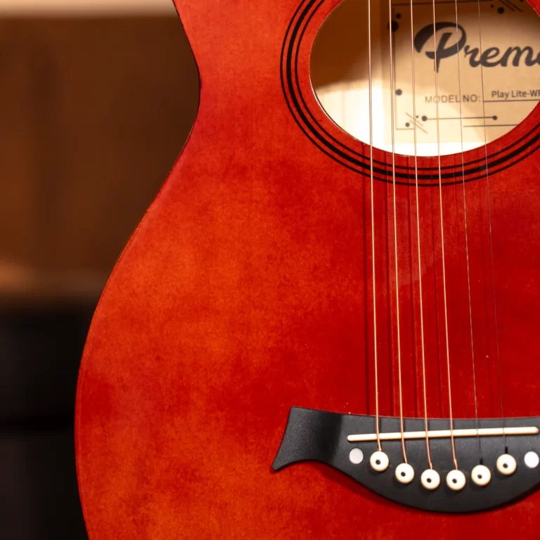 Close-up of a red-orange acoustic guitar body showing strings, bridge, and part of the soundhole label. ขายราคาพิเศษ