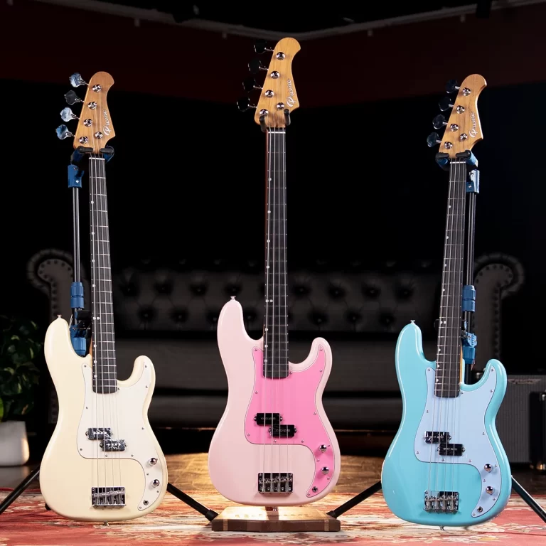 Three pastel-colored electric guitars on stands arranged in a row on a stage, left in cream, center in pink with a darker pickguard, and right in light blue against a dark backdrop. ขายราคาพิเศษ