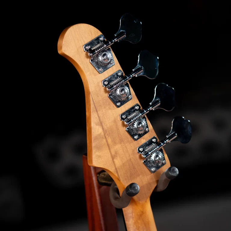 Close-up of a wooden guitar headstock with chrome tuning pegs on a stand against a dark background ขายราคาพิเศษ