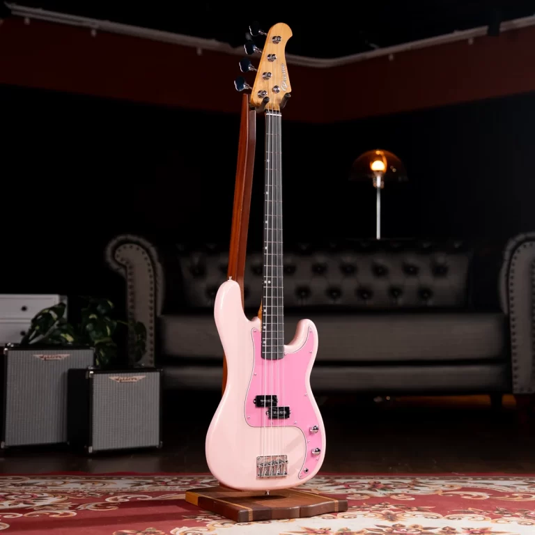 Pink electric bass guitar on a wooden stand in a cozy studio with a tufted sofa and small amplifiers in the background ขายราคาพิเศษ