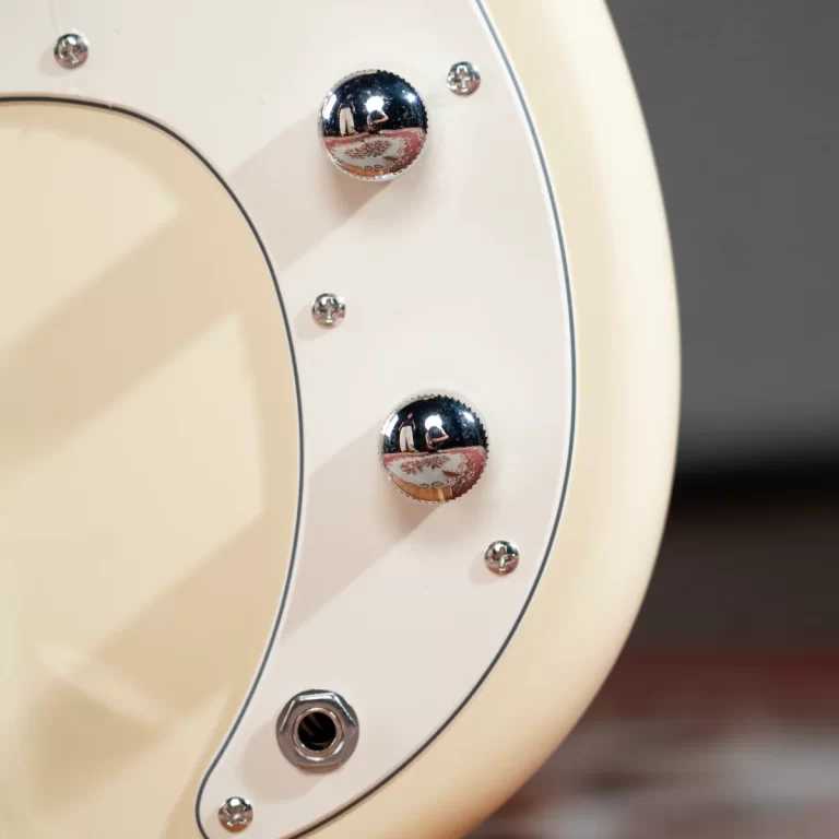 Close-up of cream electric guitar body edge showing chrome knobs and a jack input. ขายราคาพิเศษ