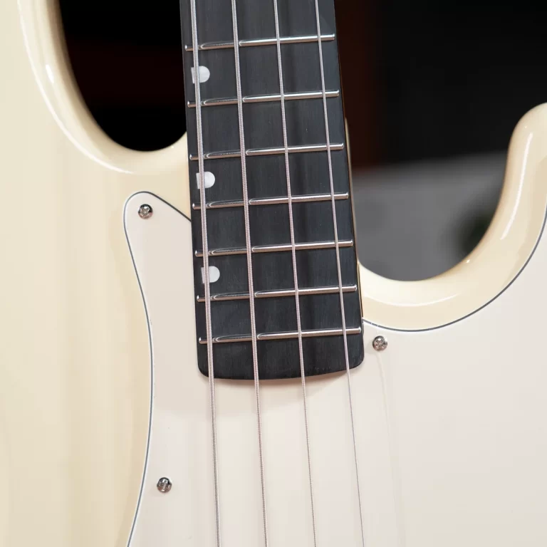 Close-up of a cream-colored electric guitar neck with metal frets and strings over a dark fretboard with a white pickguard nearby. ขายราคาพิเศษ