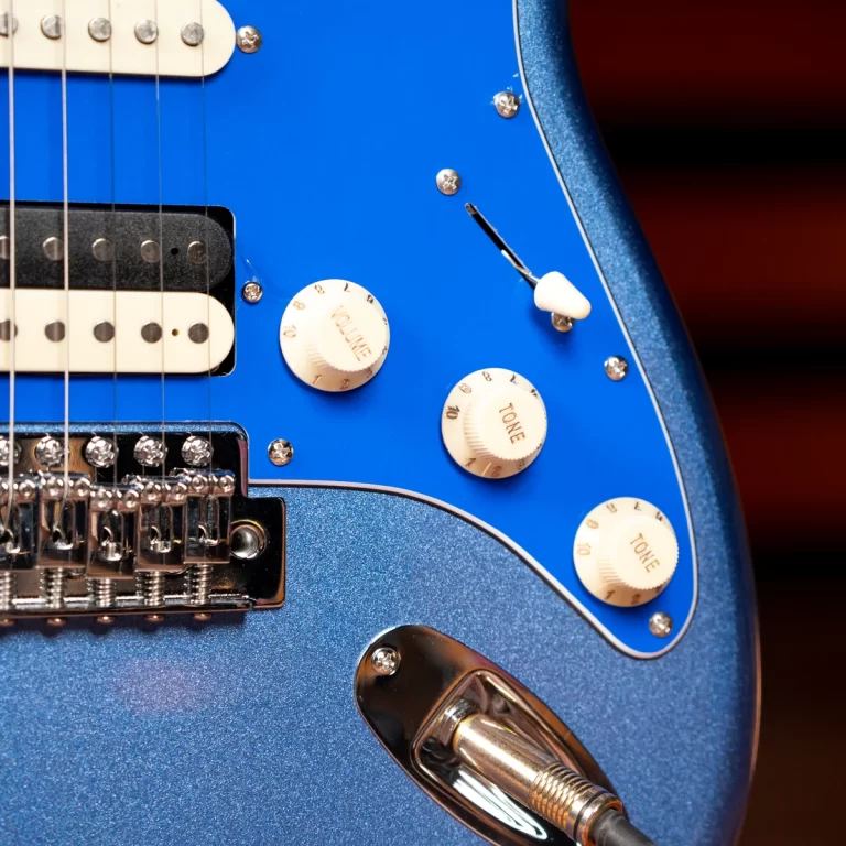 Close-up of a blue electric guitar showing volume and tone knobs and a pickup, with a plug jack at the bottom edge on a metallic blue body ขายราคาพิเศษ