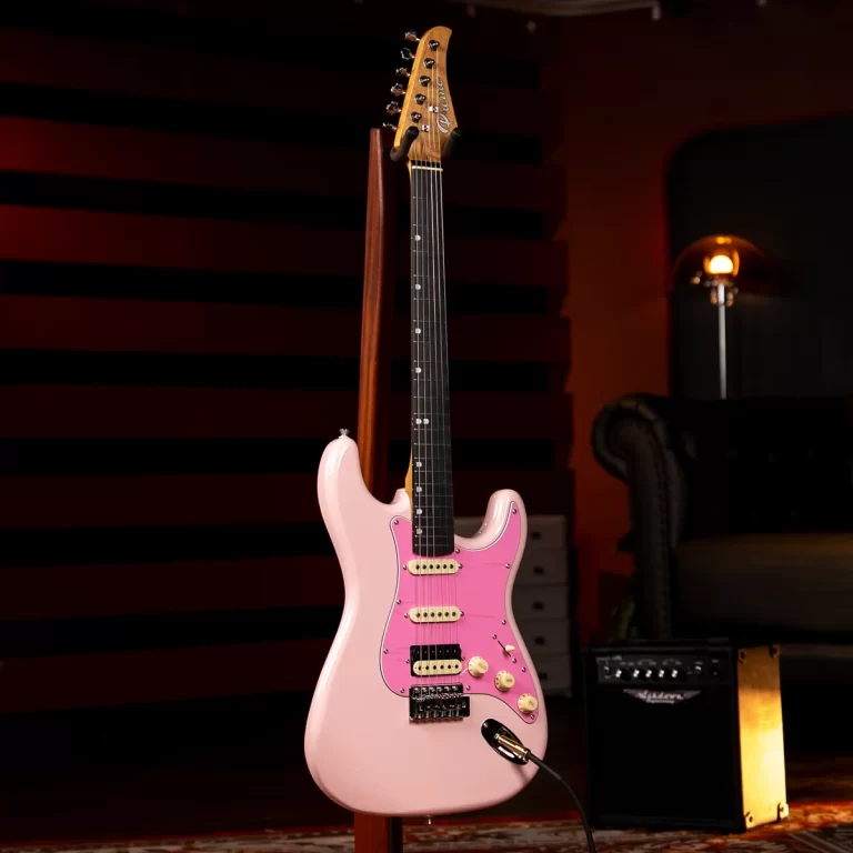 Pink Fender Strat-styled electric guitar on a stand in a dim studio with a small amp nearby and a cozy seating area in the background; guitar cable plugged in. ขายราคาพิเศษ