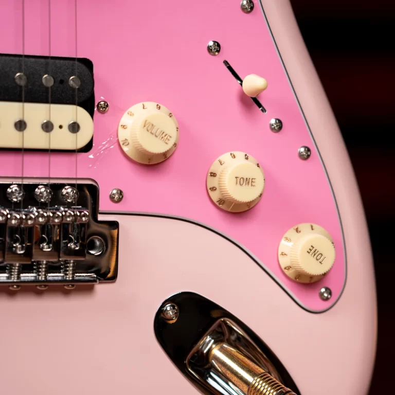 Close-up of a pink electric guitar showing cream control knobs labeled Volume and Tone and a pickup with strings nearby. ขายราคาพิเศษ
