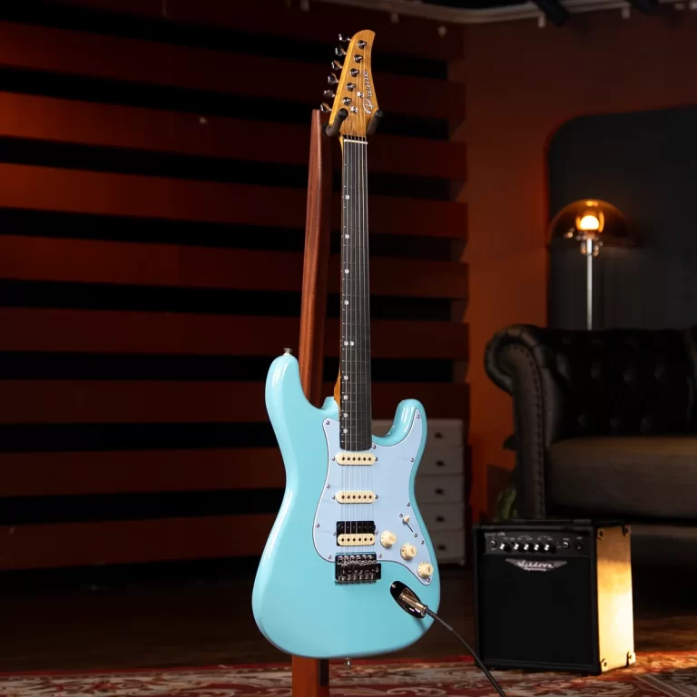 Turquoise electric guitar on a stand in a recording studio with a small amplifier nearby in the background. ขายราคาพิเศษ