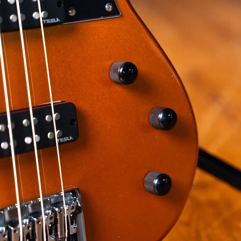 Close-up of an orange electric guitar body showing three black knurled control knobs and a two-pickup arrangement with steel strings over a chrome bridge. ขายราคาพิเศษ