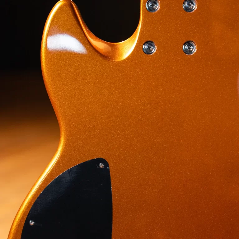 Close-up of an orange metallic guitar body with chrome screws and a black pickguard edge visible on the left. ขายราคาพิเศษ