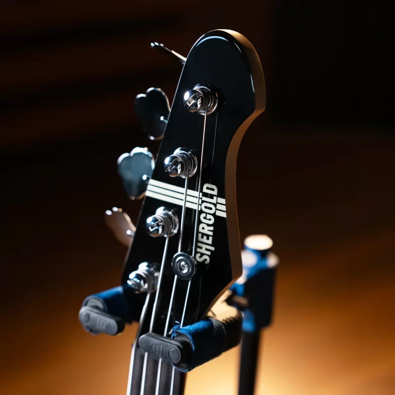 Close-up of a black guitar headstock with tuning pegs and strings, brand name SHERGOLD visible, mounted on a stand in a dimly lit setting. ขายราคาพิเศษ