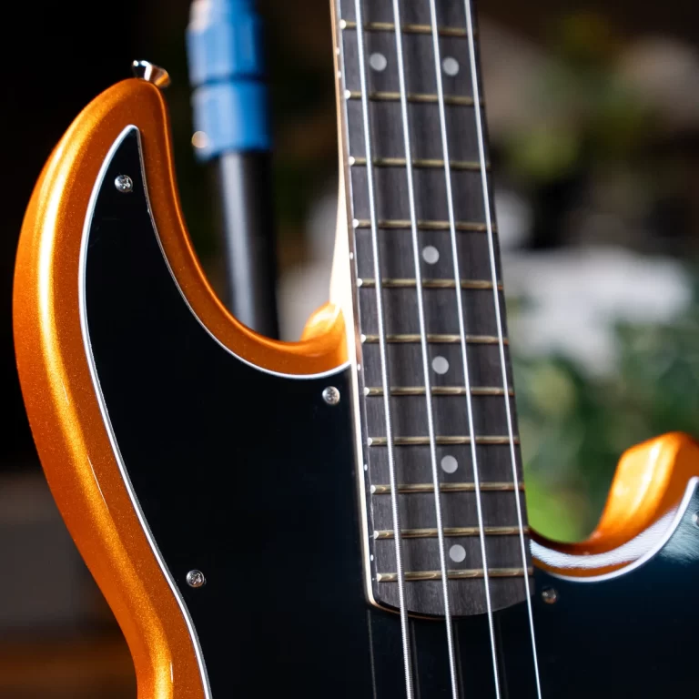 Close-up of an orange electric guitar body with a black pickguard and metal strings on the fretboard. ขายราคาพิเศษ