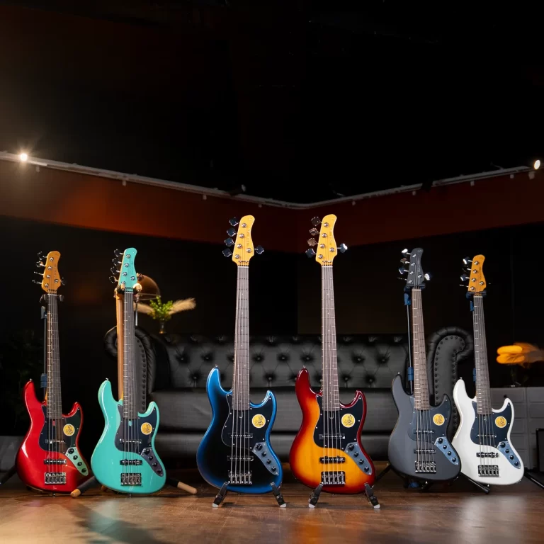 Row of colorful bass guitars on stands in a showroom or studio with a tufted sofa in the background ขายราคาพิเศษ
