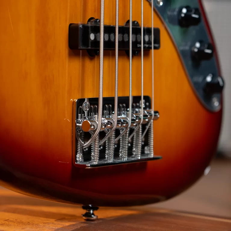 Close-up of a sunburst electric bass showing the chrome bridge, saddles, and steel strings in focus on a wooden body. ขายราคาพิเศษ