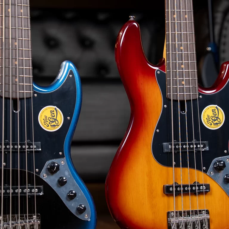 Two electric bass guitars side by side: blue on the left and sunburst red on the right, each with a sticker and visible pickups and controls. ขายราคาพิเศษ