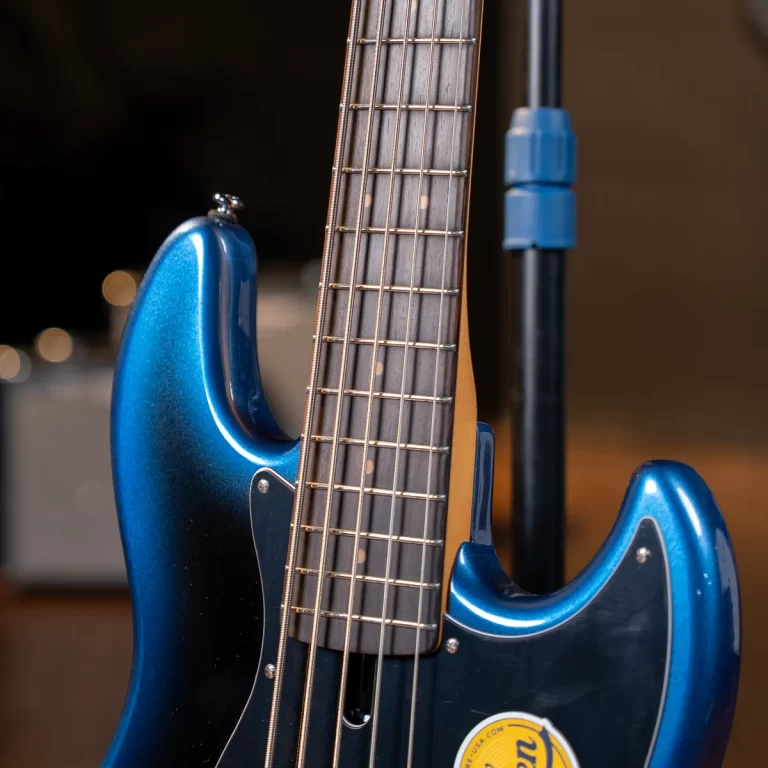 Blue glossy electric bass guitar close-up showing the neck, frets, and strings with a microphone stand in the background in a studio setting. ขายราคาพิเศษ