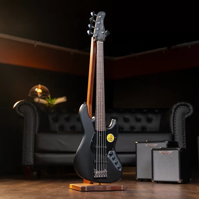 Black electric guitar on a wooden stand in a dim studio with two small amps to the right and a tufted sofa in the background ขายราคาพิเศษ