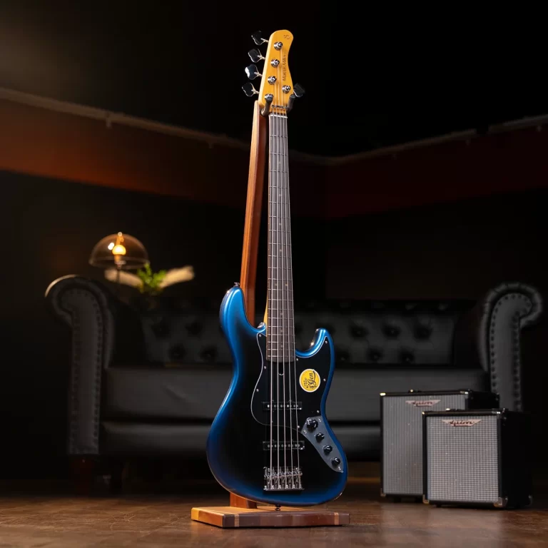 Blue electric bass guitar on a wooden stand in a dim studio, with small amplifiers in the background behind a sofa. ขายราคาพิเศษ