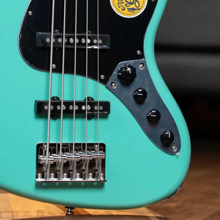 Turquoise electric bass guitar close-up showing strings, pickups, and chrome bridge on a black pickguard edge. ขายราคาพิเศษ