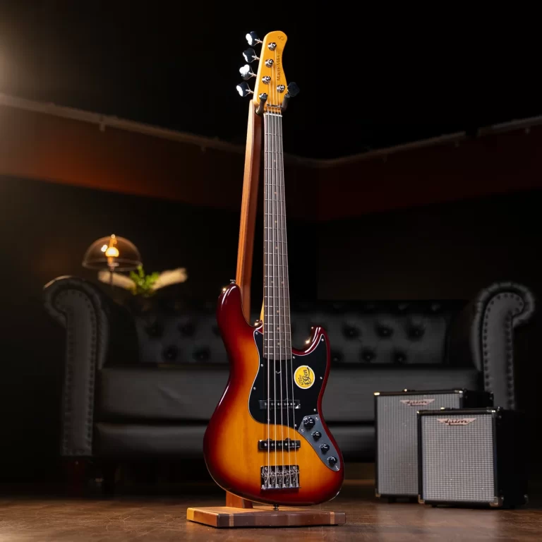 Sunburst electric bass on a stand in a dim studio, with two guitar amplifiers in the background. ขายราคาพิเศษ