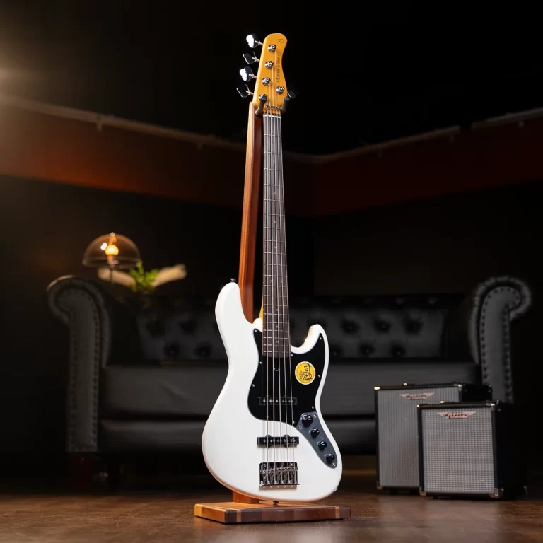 White electric guitar on a wooden stand in a dim room with a tufted gray sofa in the background and small amplifiers to the right. ขายราคาพิเศษ