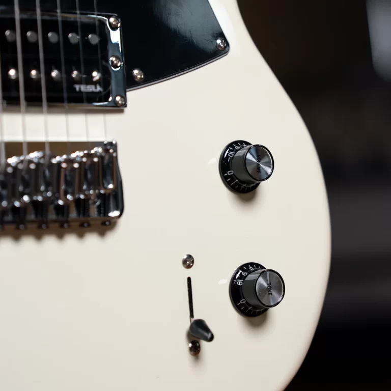 Close-up of a white electric guitar body with two black control knobs (volume and tone), a chrome bridge, and a toggle switch. ขายราคาพิเศษ