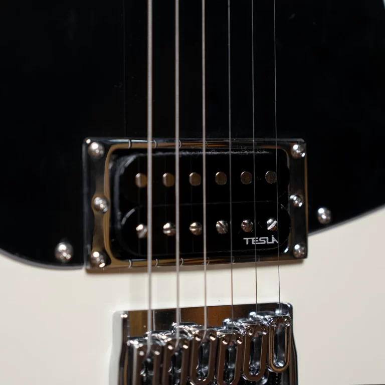 Close-up of a black electric guitar pickup and six steel strings over a chrome bridge. The pickup has a TESLA logo visible on its cover. ขายราคาพิเศษ