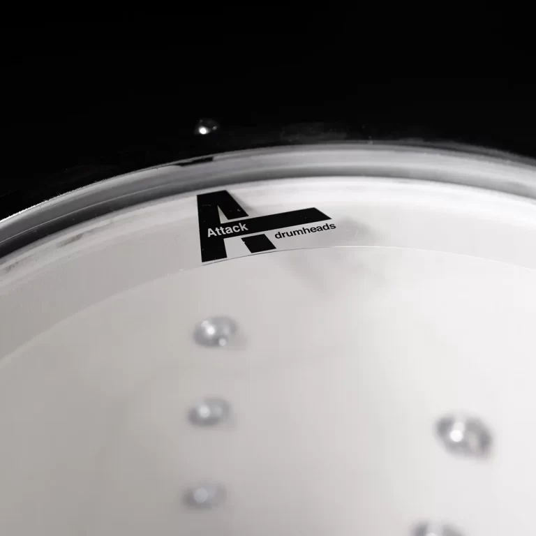 Close-up of a white drumhead with the black 'Attack drumheads' logo on a dark background. ขายราคาพิเศษ