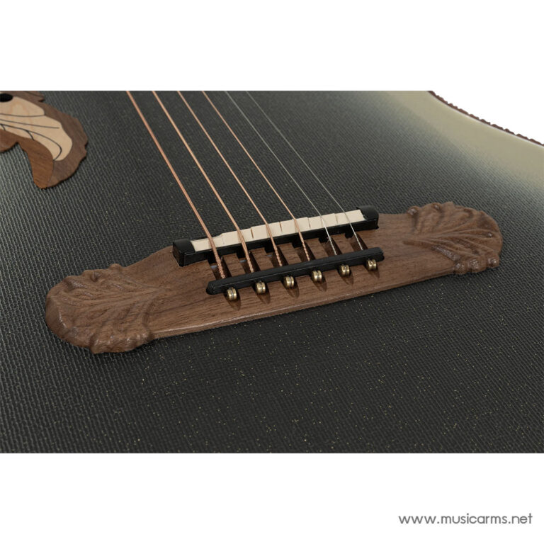 Close-up of an acoustic guitar bridge with six strings and a carved wooden tailpiece on a textured surface. ขายราคาพิเศษ