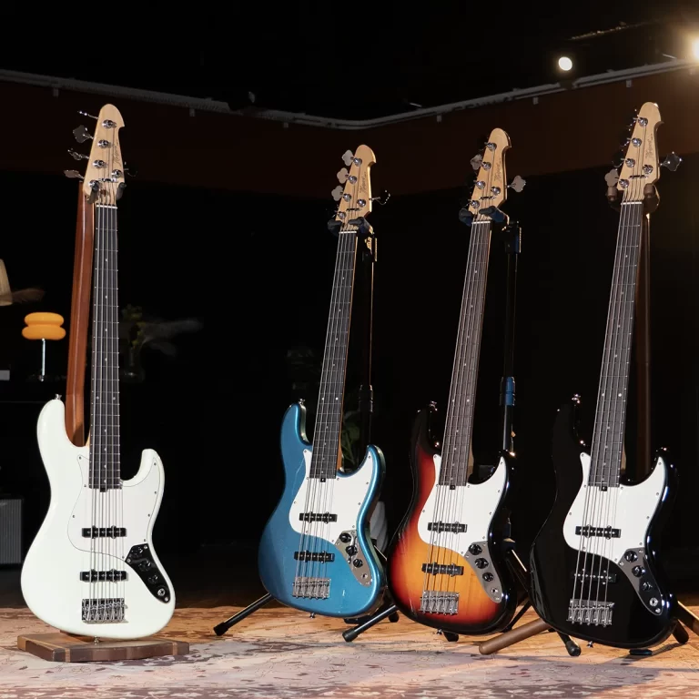 Four bass guitars on stands on a dim stage: white, teal, sunburst, and black finishes. ขายราคาพิเศษ
