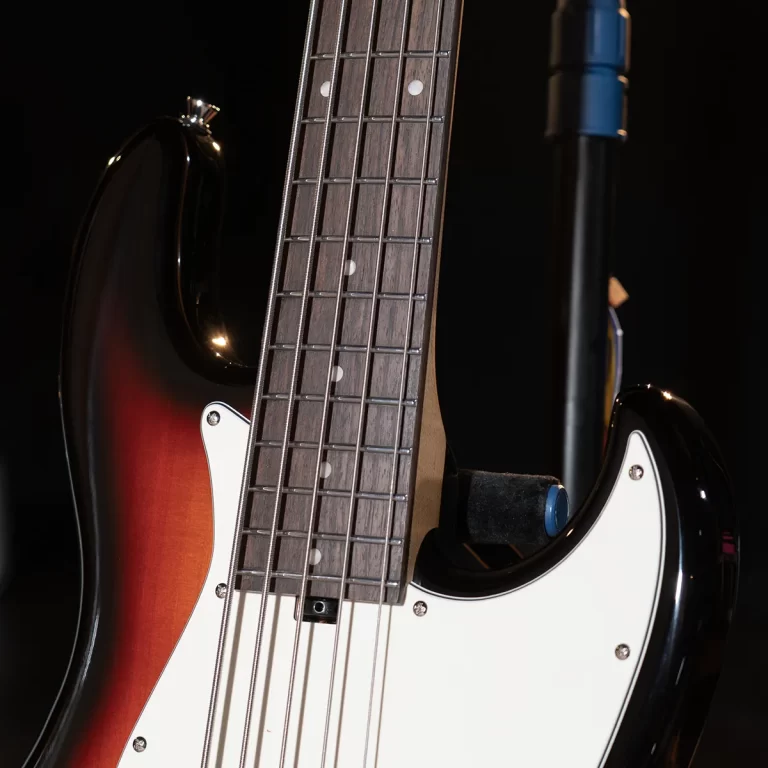 Close-up of a sunburst electric bass guitar with a white pickguard and fretboard details against a dark background, showing strings and pickups. ขายราคาพิเศษ
